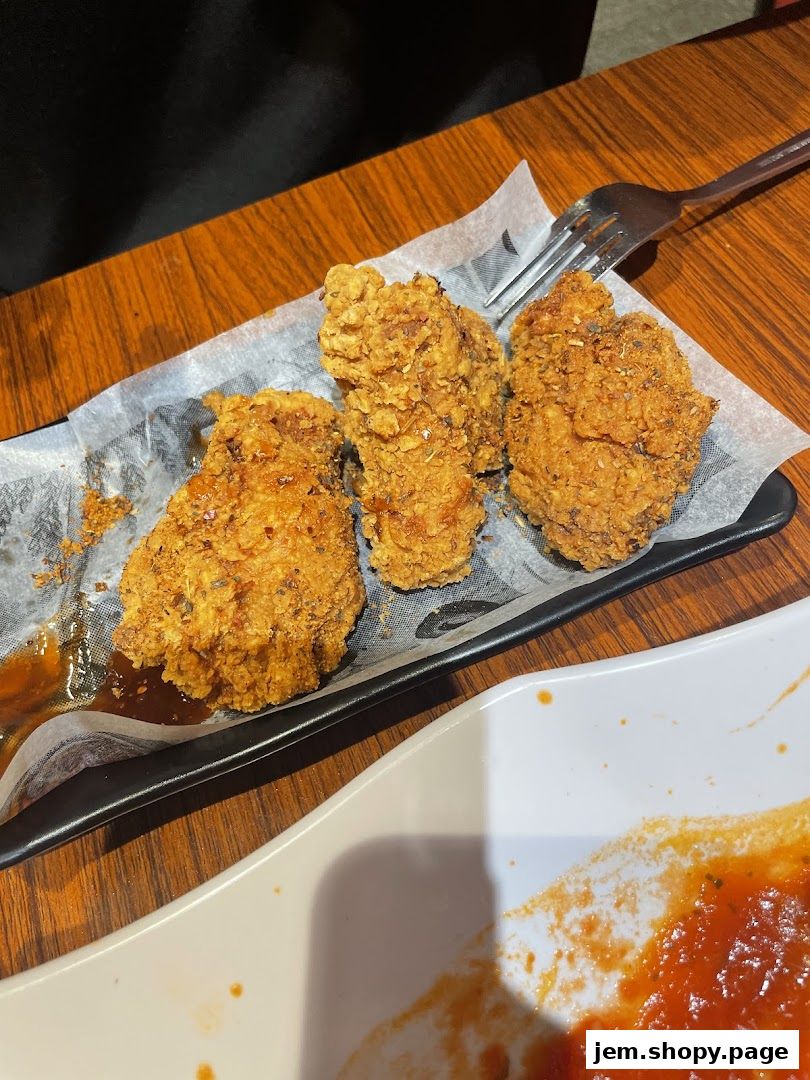 Crispy fried chicken pieces served on a black plate with a fork and sauce.