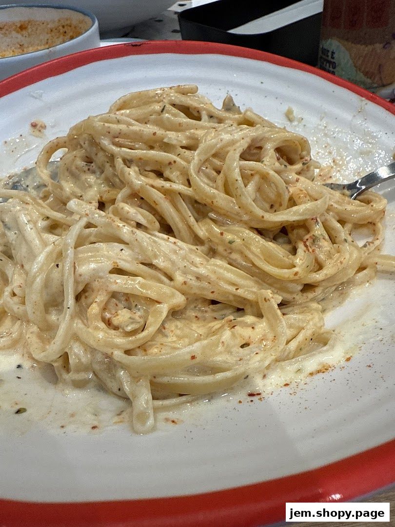 A close-up shot of a creamy pasta dish served on a white plate with a red rim.