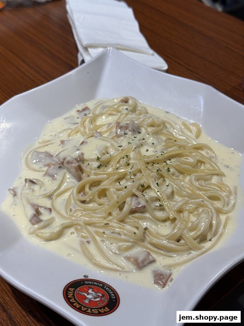 A close-up shot of a creamy pasta dish with bacon bits served in a white bowl.
