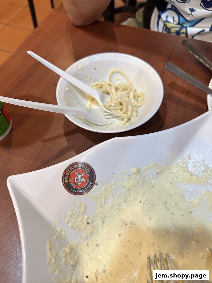 A partially eaten pasta dish with plastic cutlery on a wooden table.