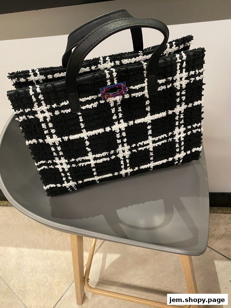 A black and white plaid textured handbag with leather handles sits on a grey chair.