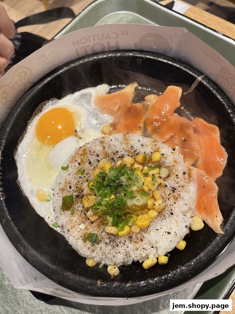 A sizzling hot plate of rice with salmon, a fried egg, and corn, garnished with green onions.
