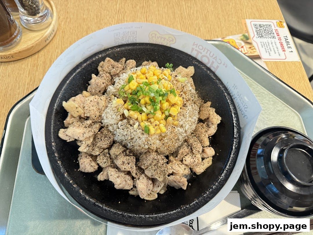 A sizzling hot plate of chicken and rice topped with corn and green onions.