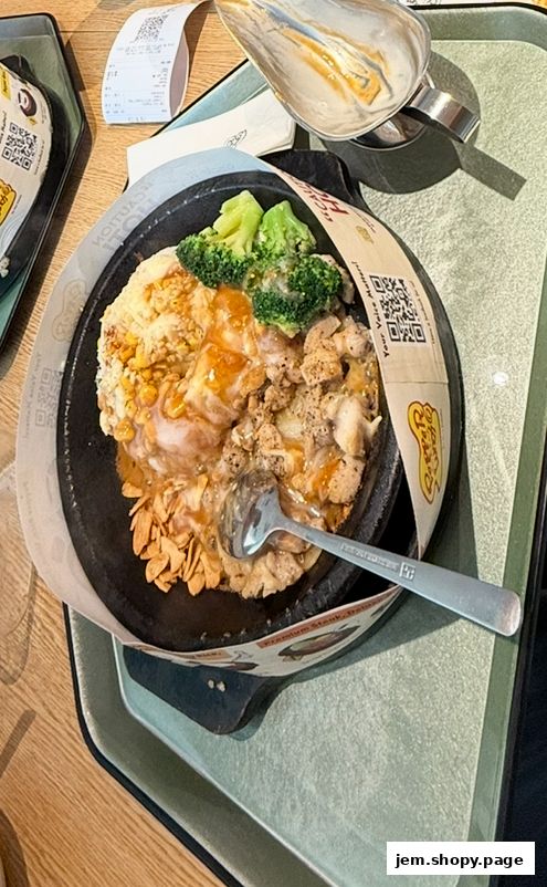 A sizzling hot plate meal with chicken, broccoli, rice, and fried garlic.