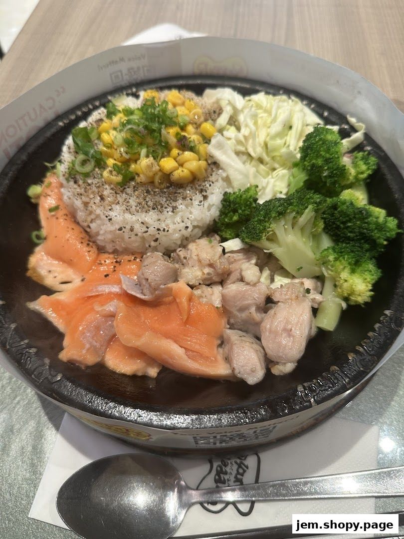 A sizzling hot plate meal with rice, salmon, chicken, corn, cabbage, and broccoli.