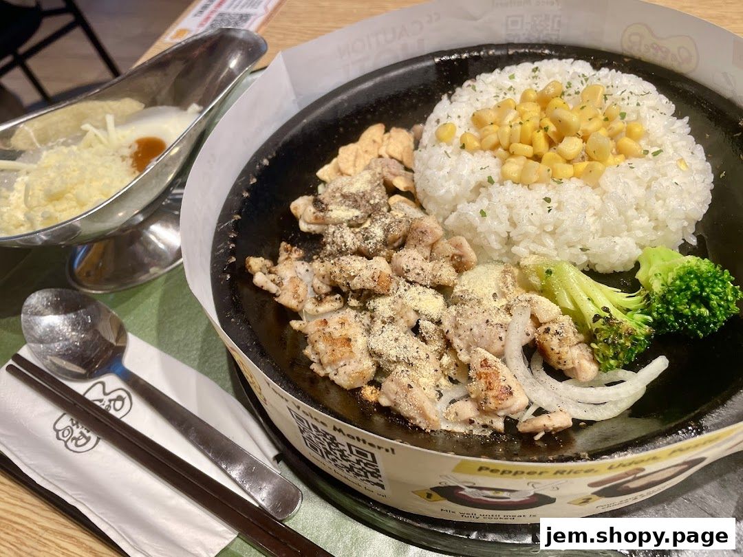 A sizzling hot plate meal with chicken, rice, corn, broccoli, and a side of cheese sauce.