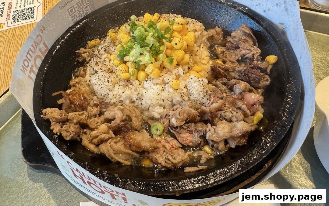A sizzling hot plate of rice with beef and corn, garnished with green onions.