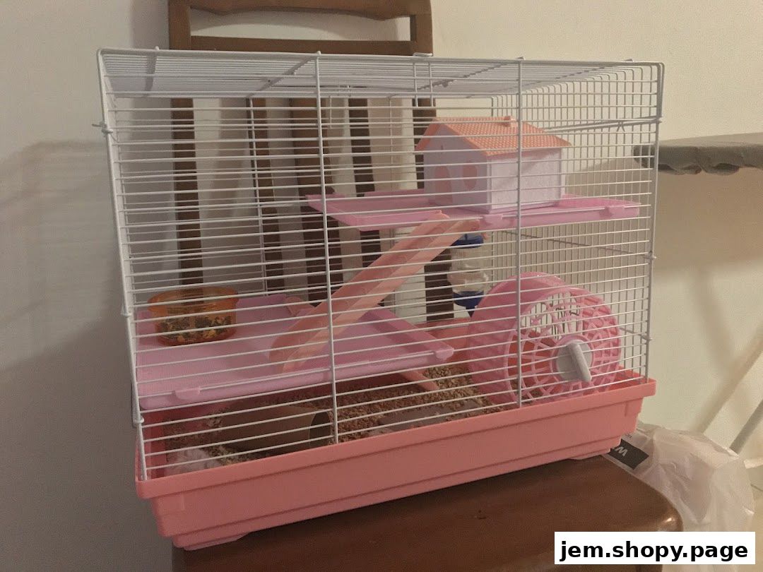 A pink multi-level hamster cage with accessories, including a house, wheel, and food dish.