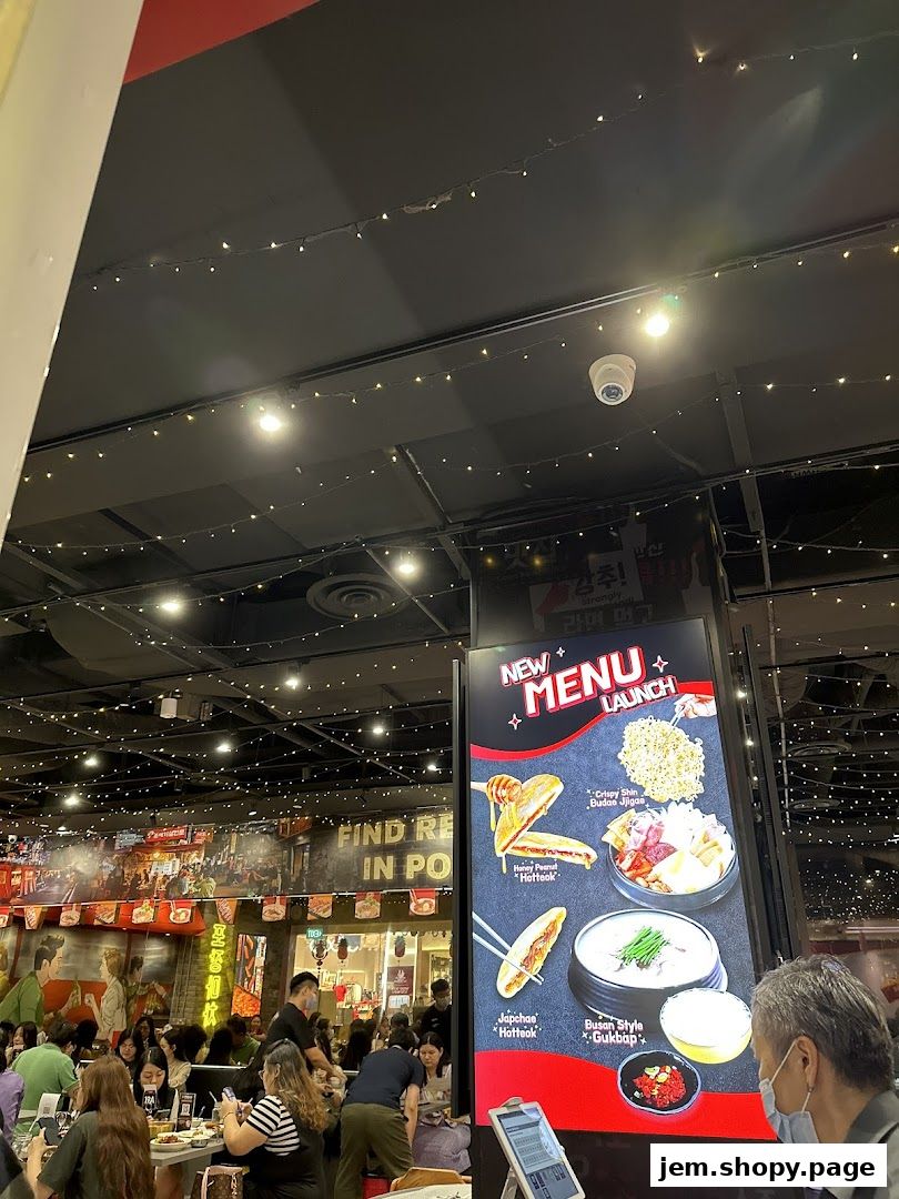 A lively interior of a Korean street dining restaurant with customers and a new menu display.