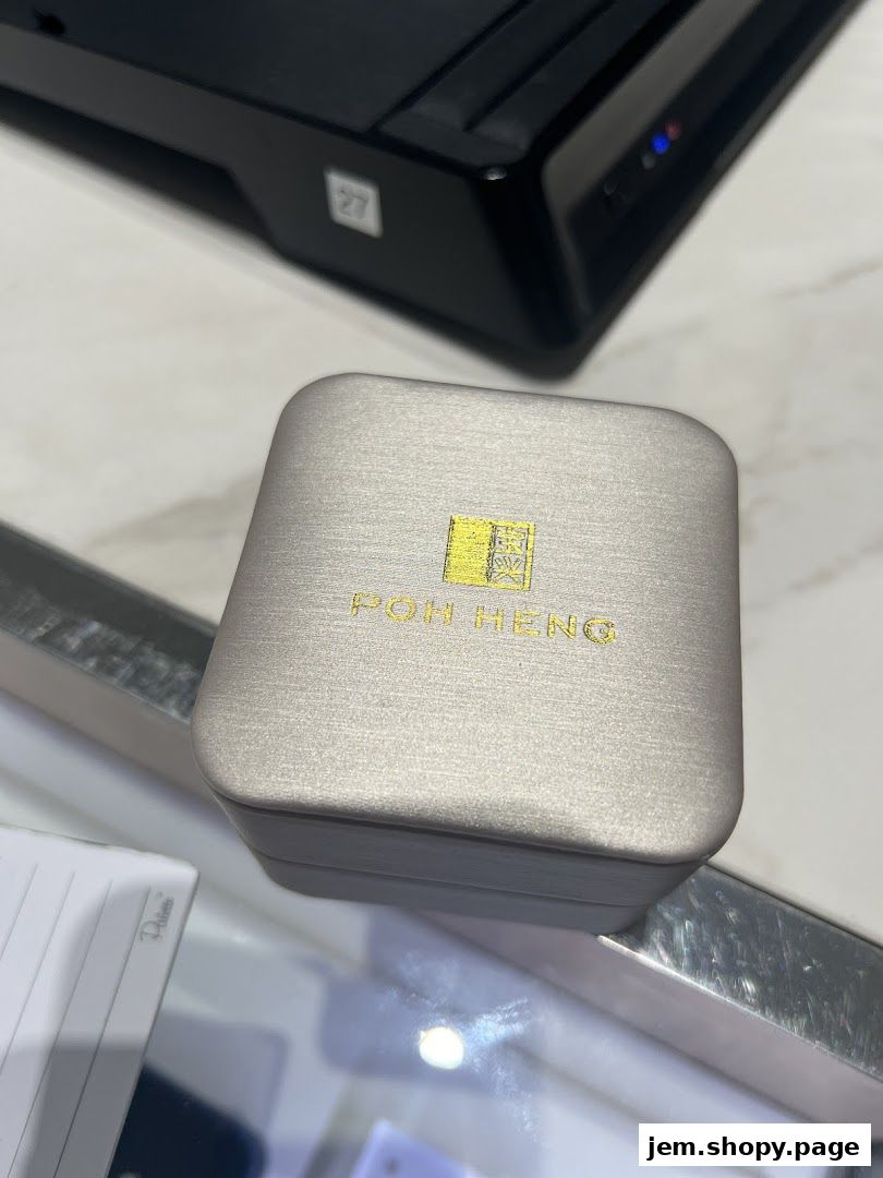 A close-up of a Poh Heng Jewellery branded box on a reflective surface.