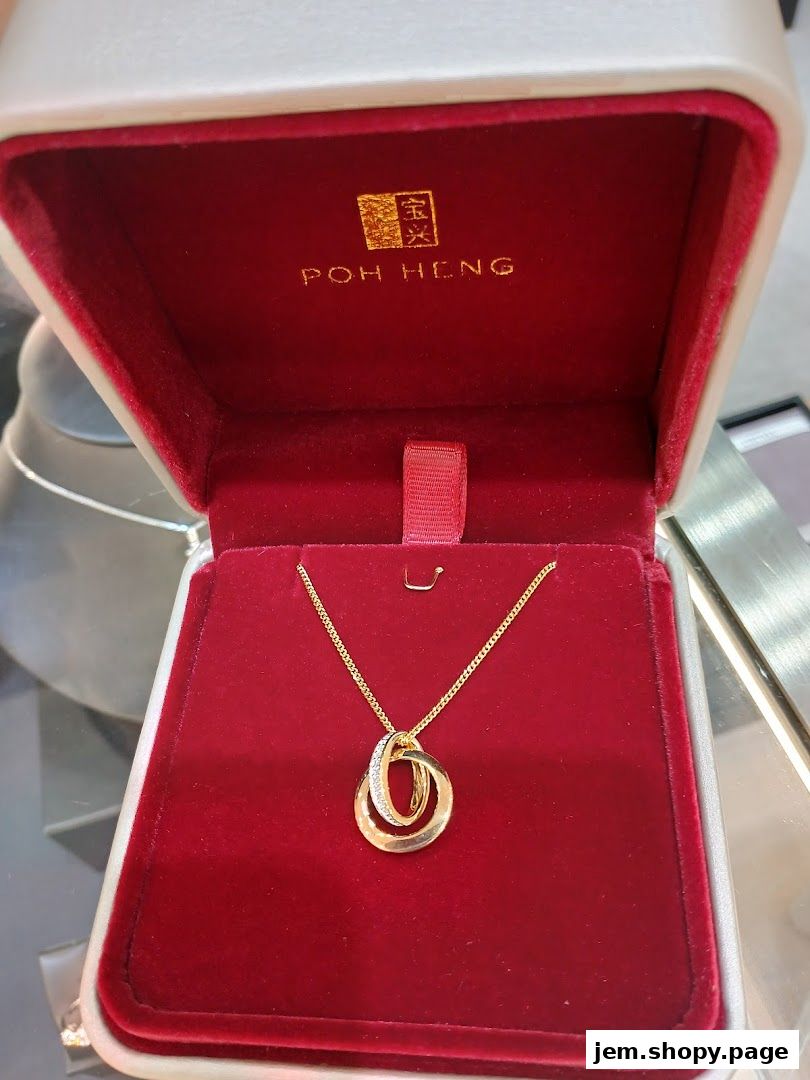 A gold necklace with interlocking rings, one adorned with diamonds, displayed in a Poh Heng Jewellery box.