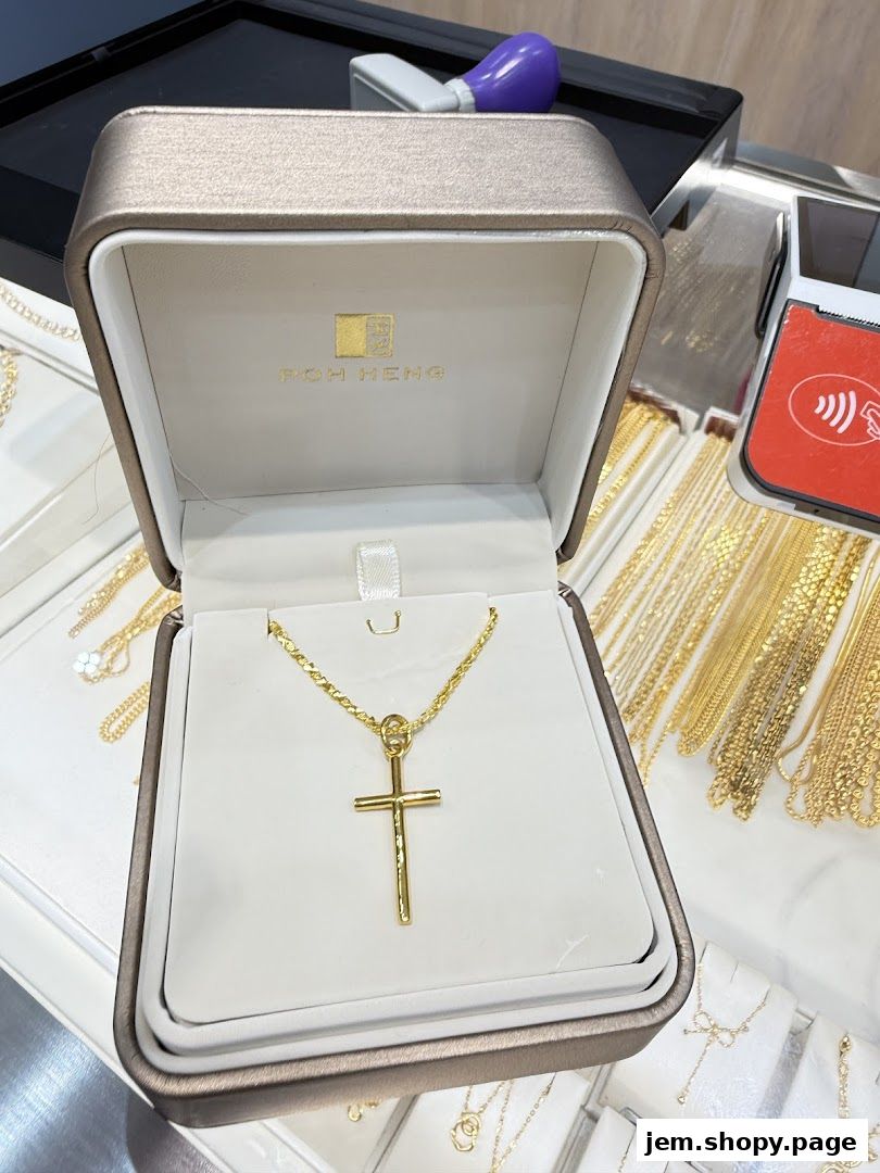 A gold cross pendant necklace displayed in a Poh Heng Jewellery box.