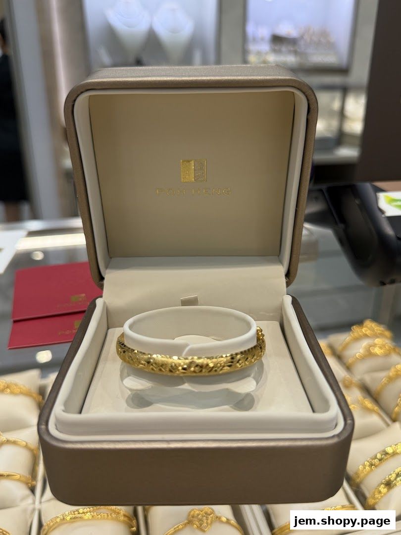 A gold bracelet displayed in an open box with the Poh Heng logo.