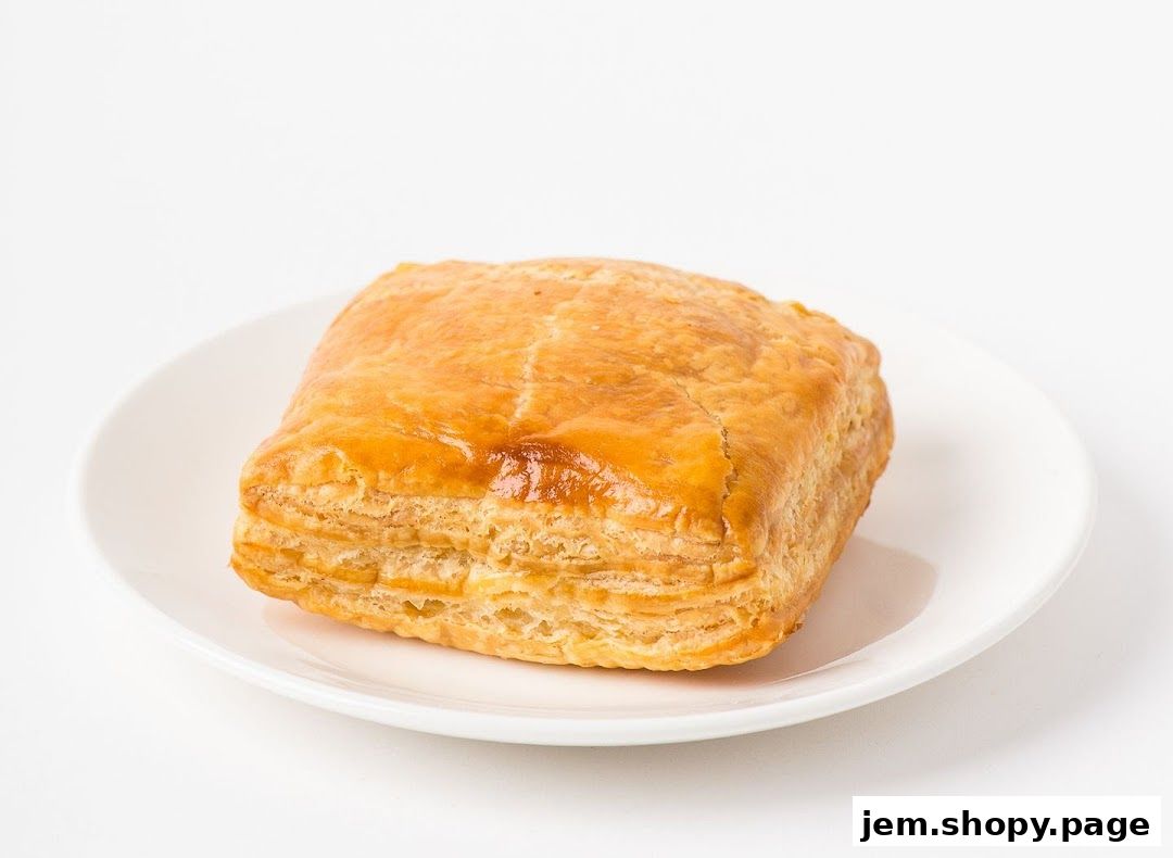 A golden-brown puff pastry on a white plate against a white background.