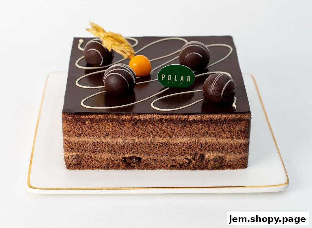 A decadent chocolate cake with chocolate truffles and a golden garnish on a white plate.