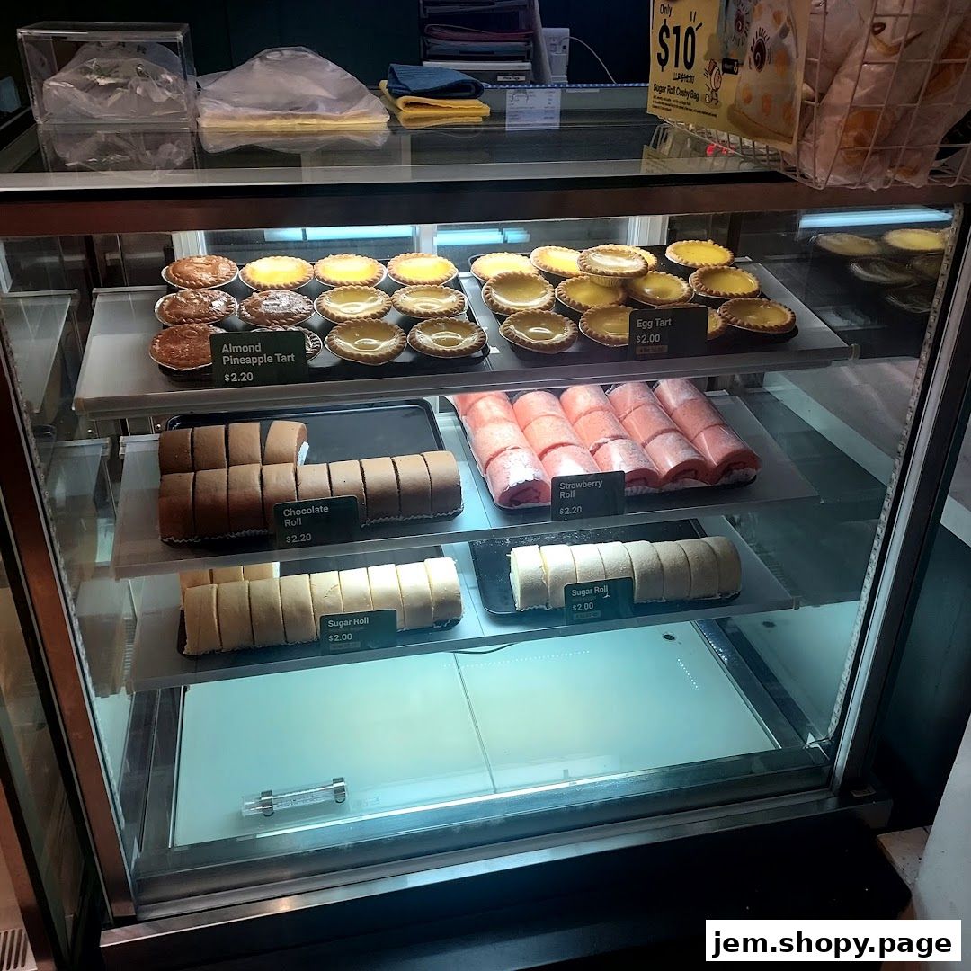 A display case filled with various pastries including tarts and swiss rolls.
