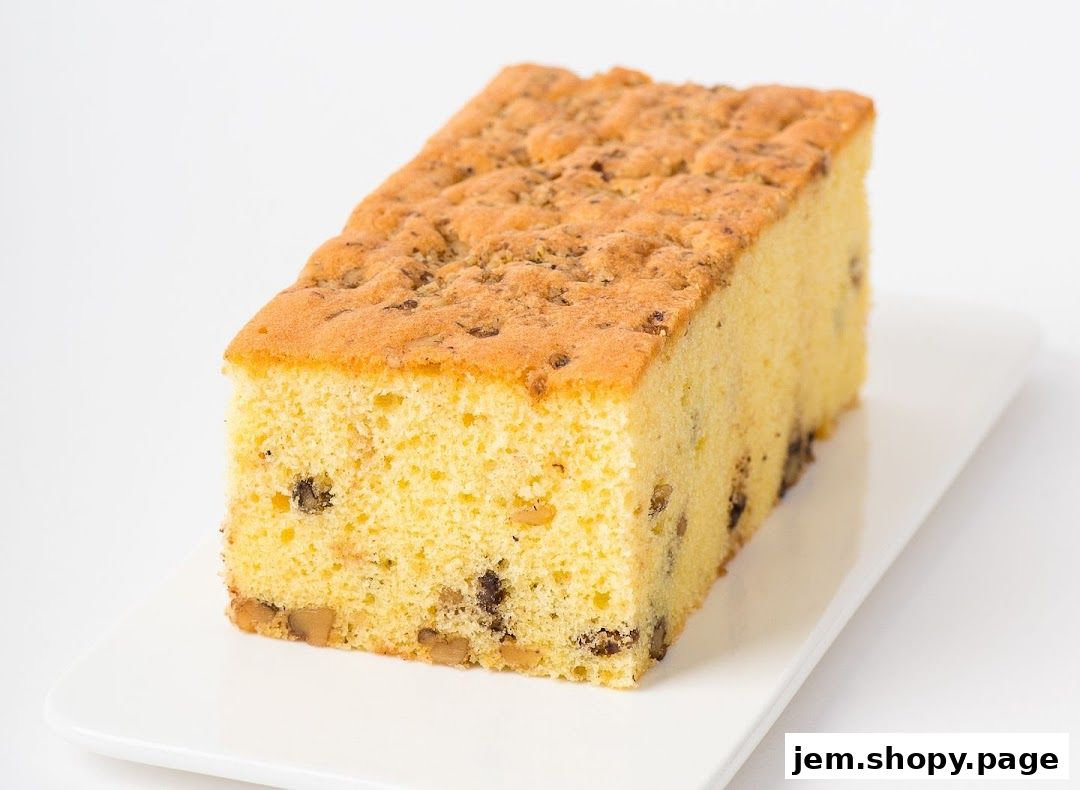 A slice of moist cake with nuts and chocolate chips on a white plate.