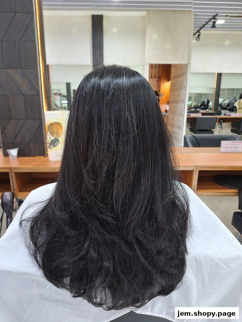 Back view of a person with long, dark, layered hair in a salon.