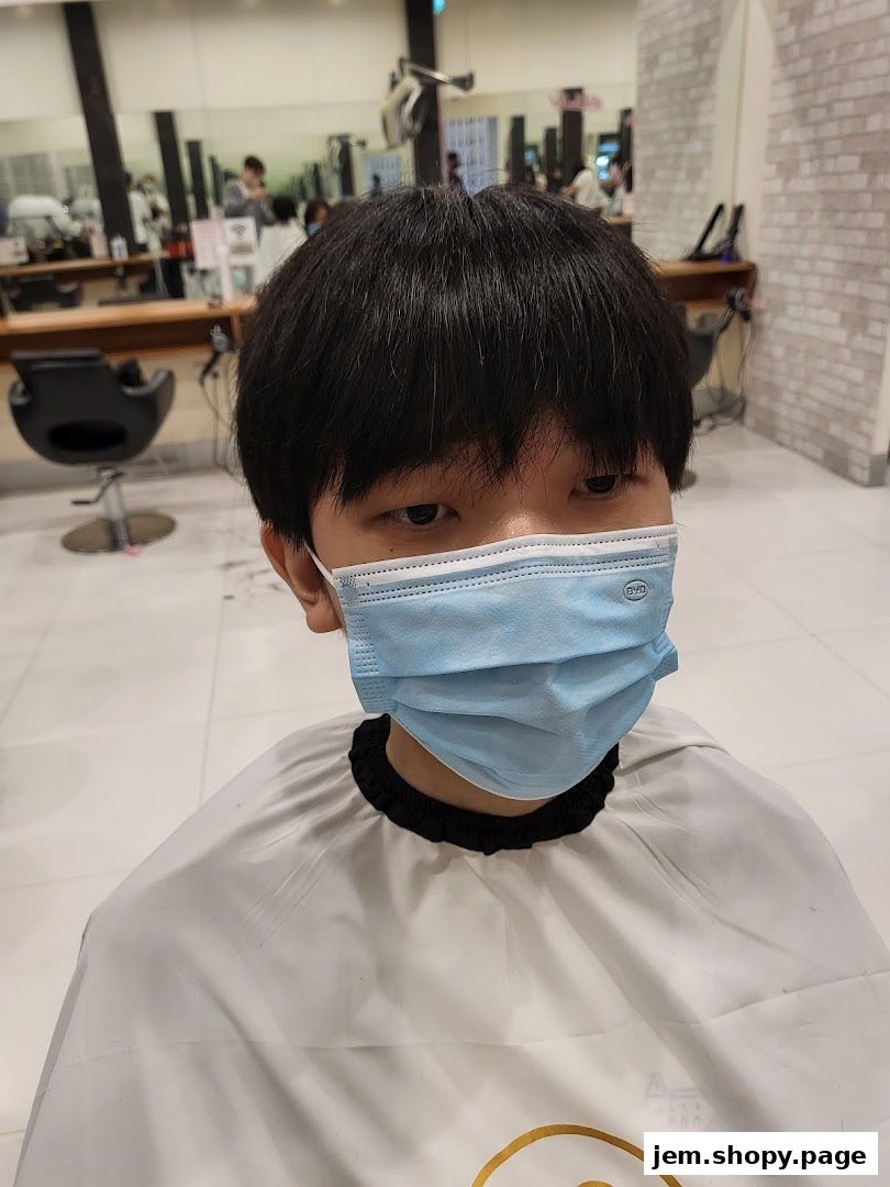 A person wearing a mask and salon cape in a hair salon.