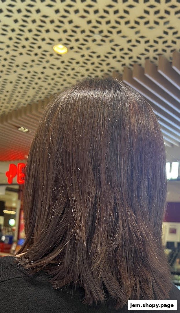 Back view of a person with dark, shoulder-length hair in a brightly lit salon.