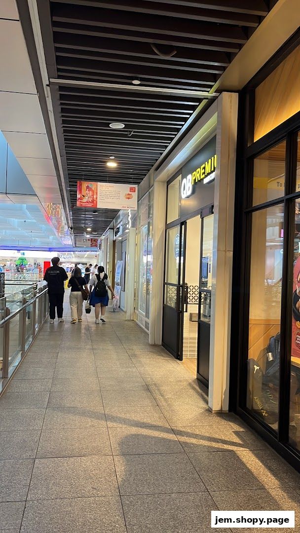 A shopping mall corridor with people walking past the entrance of QB PREMIUM JEM.