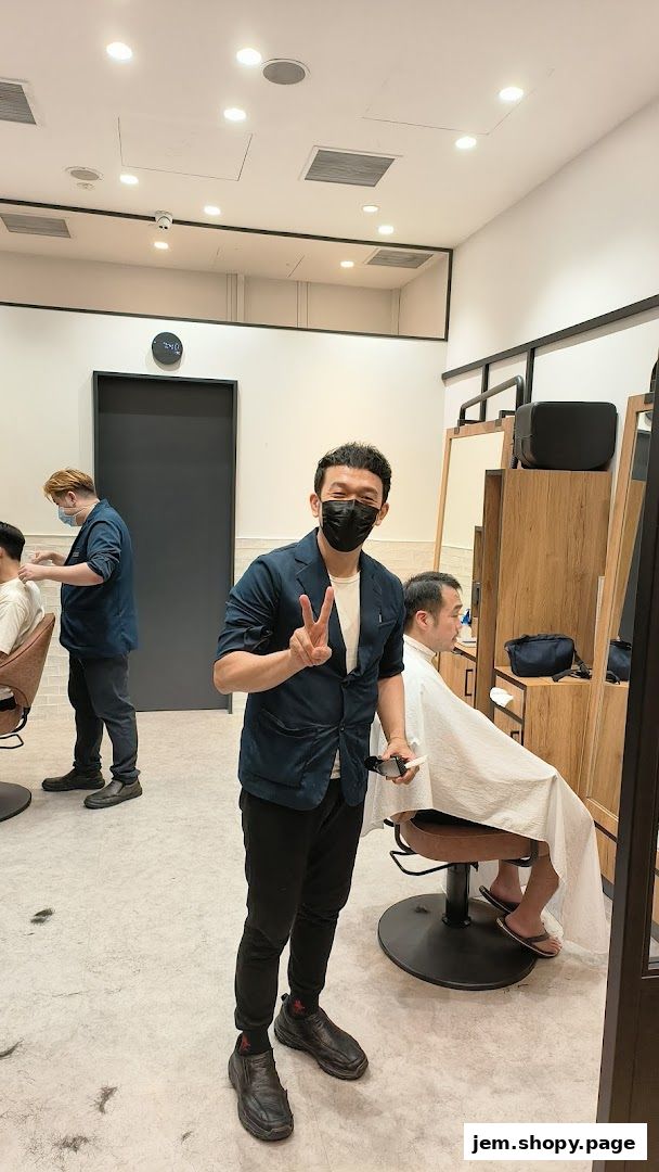 A barber smiles and makes a peace sign while holding clippers in a modern barbershop.