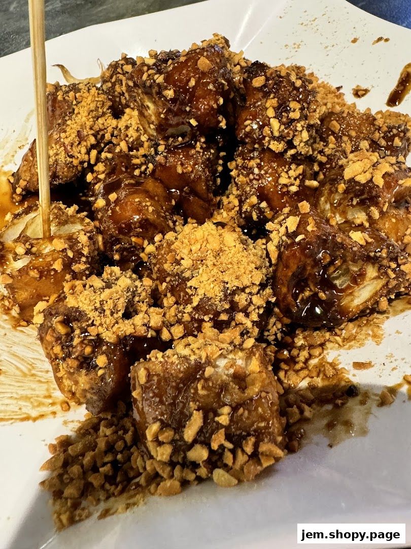 A plate of fried food coated in a dark sauce and sprinkled with chopped nuts.