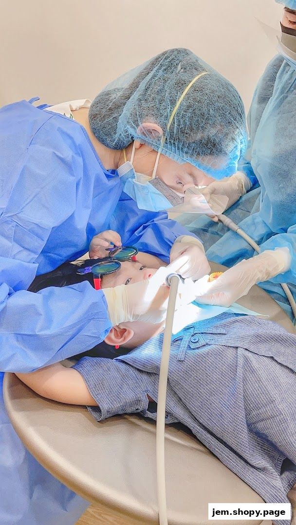 Dentists in protective gear examine a child's teeth with dental tools.
