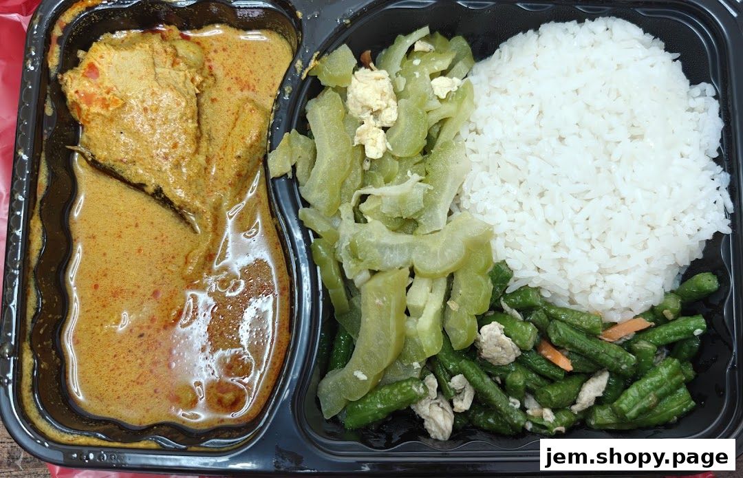 A takeaway container filled with rice, curry chicken, stir-fried bitter gourd, and green beans.