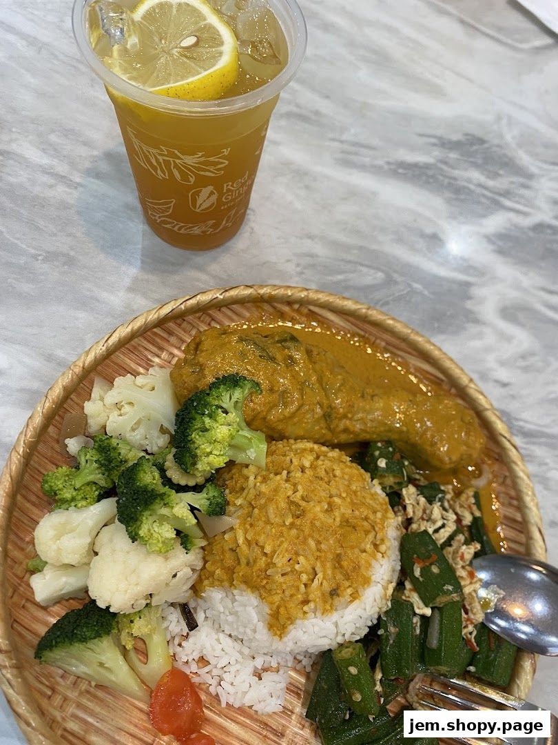 A plate of rice with curry chicken, vegetables, and a lemon drink.