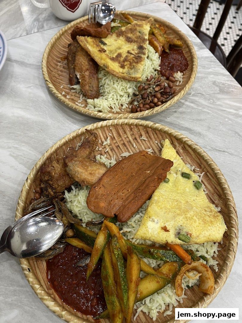 Two plates of nasi lemak with fried chicken, omelette, and sambal served on woven platters.