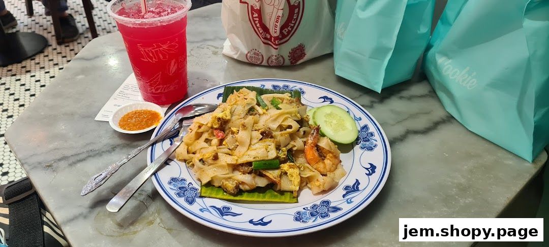 A plate of stir-fried noodles with shrimp, a drink, and takeaway bags on a marble table.