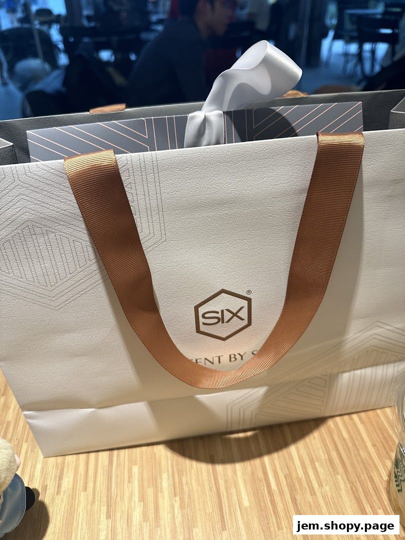 A white shopping bag with a logo and ribbon from Scent by SIX.