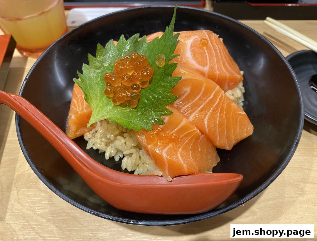 A close-up of a salmon donburi with ikura, served in a black bowl with a red spoon.