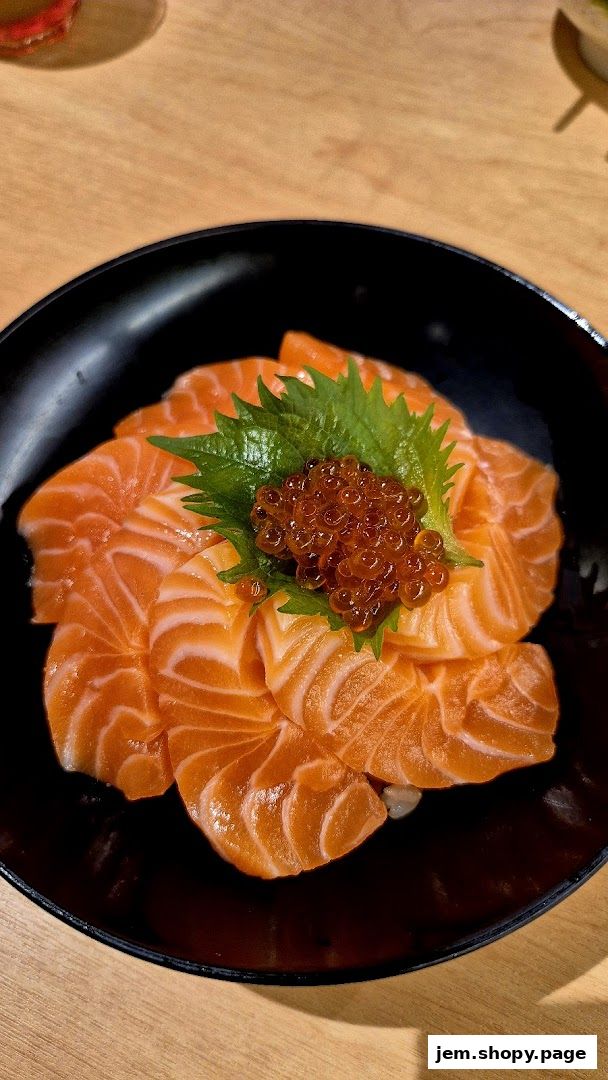 A close-up of a salmon donburi with ikura and shiso leaf in a black bowl.