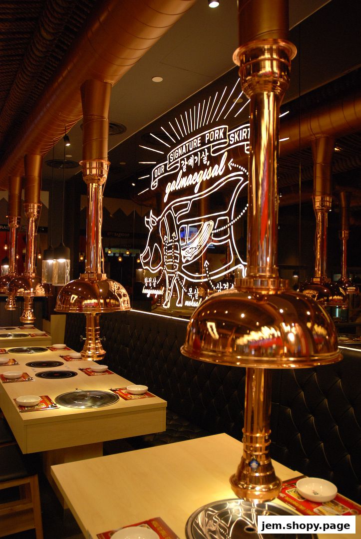 Interior of a Korean BBQ restaurant with copper ventilation hoods and tables set for dining.