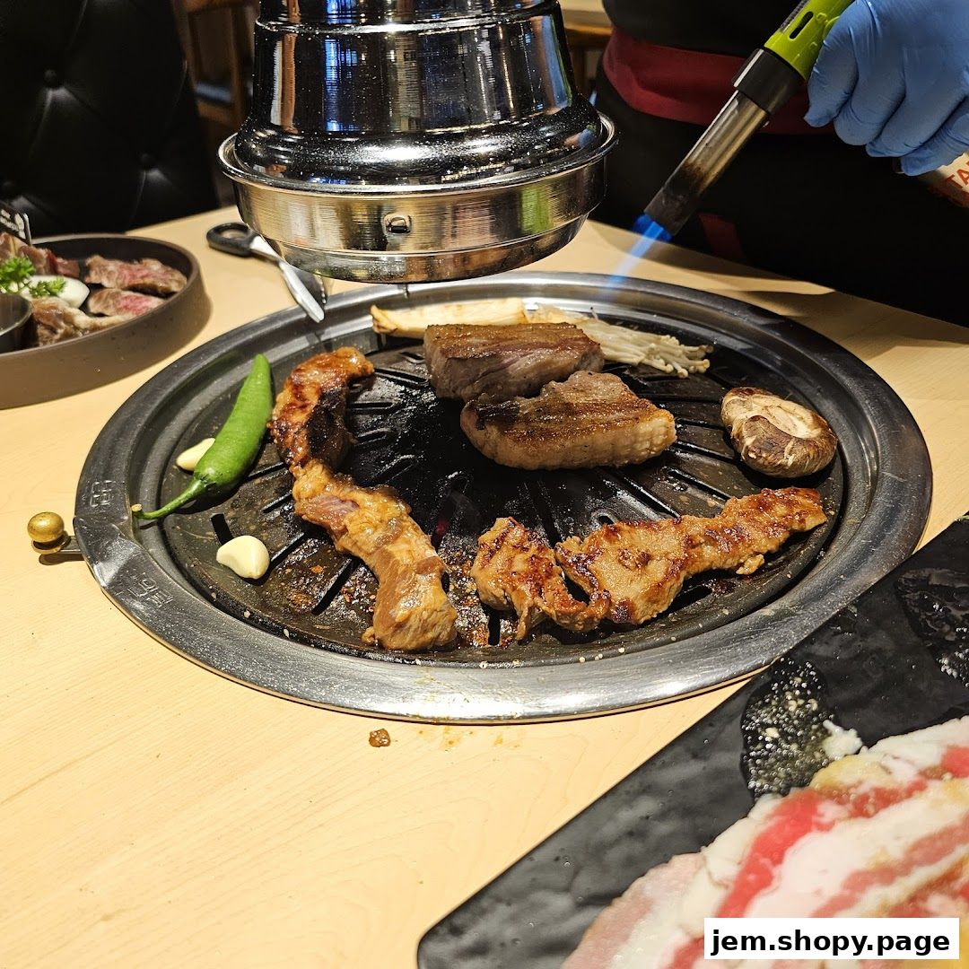 Meat and vegetables are grilled on a table-top grill with a torch.