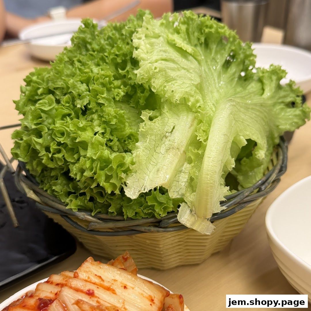 A basket of fresh green lettuce leaves sits on a table next to kimchi.