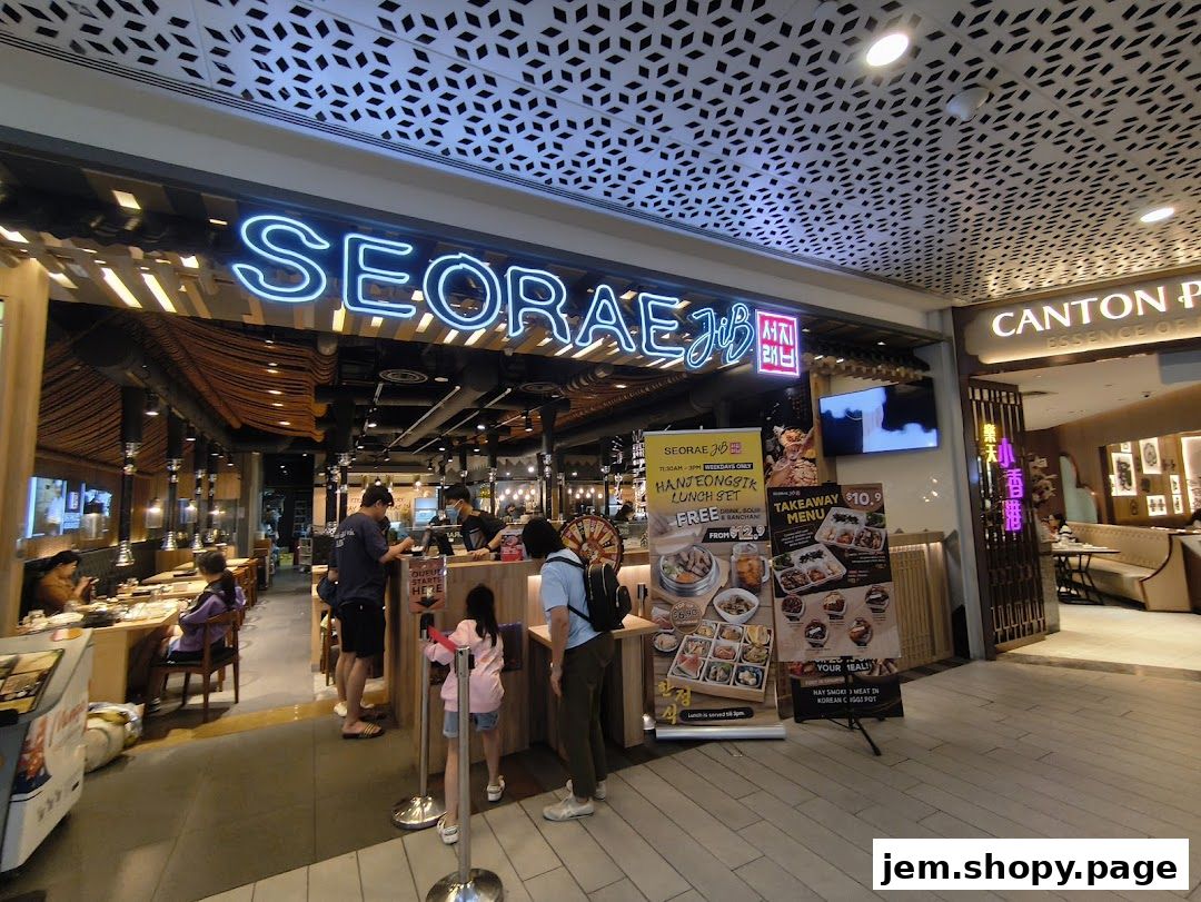 The exterior of a Korean restaurant, SEORAE JIB JEM, with neon signage and promotional posters.