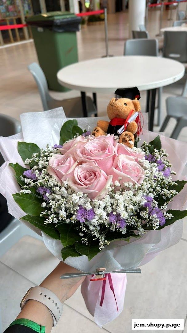 A hand holds a bouquet of pink roses and baby's breath with a graduation teddy bear.