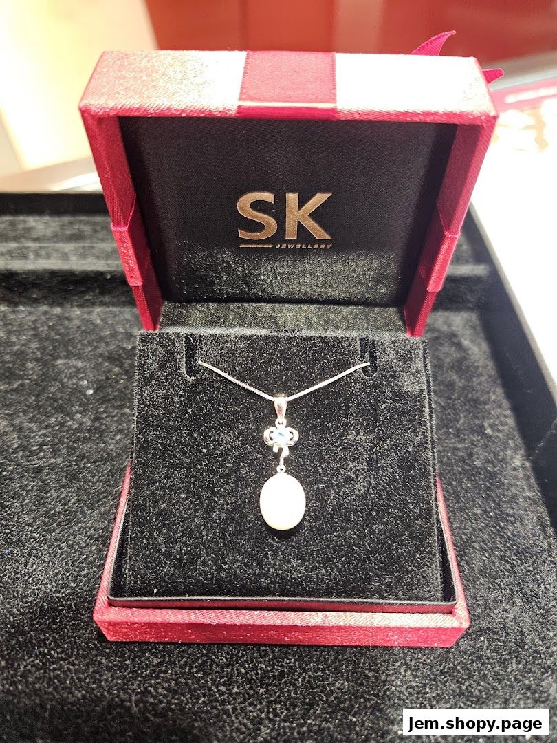 A pearl pendant necklace displayed in an open red jewelry box with the SK Jewellery logo.