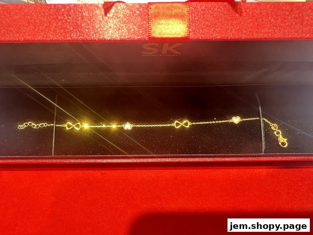 A gold bracelet with infinity and heart charms displayed in a red gift box.