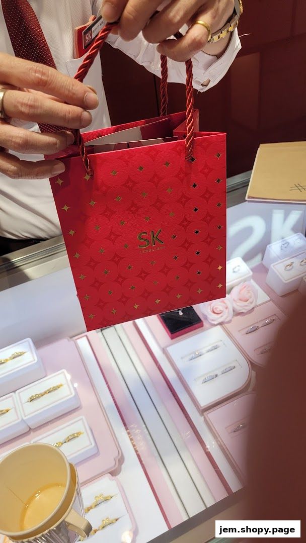 A person holds a red SK Jewellery gift bag over a display of rings and jewelry.
