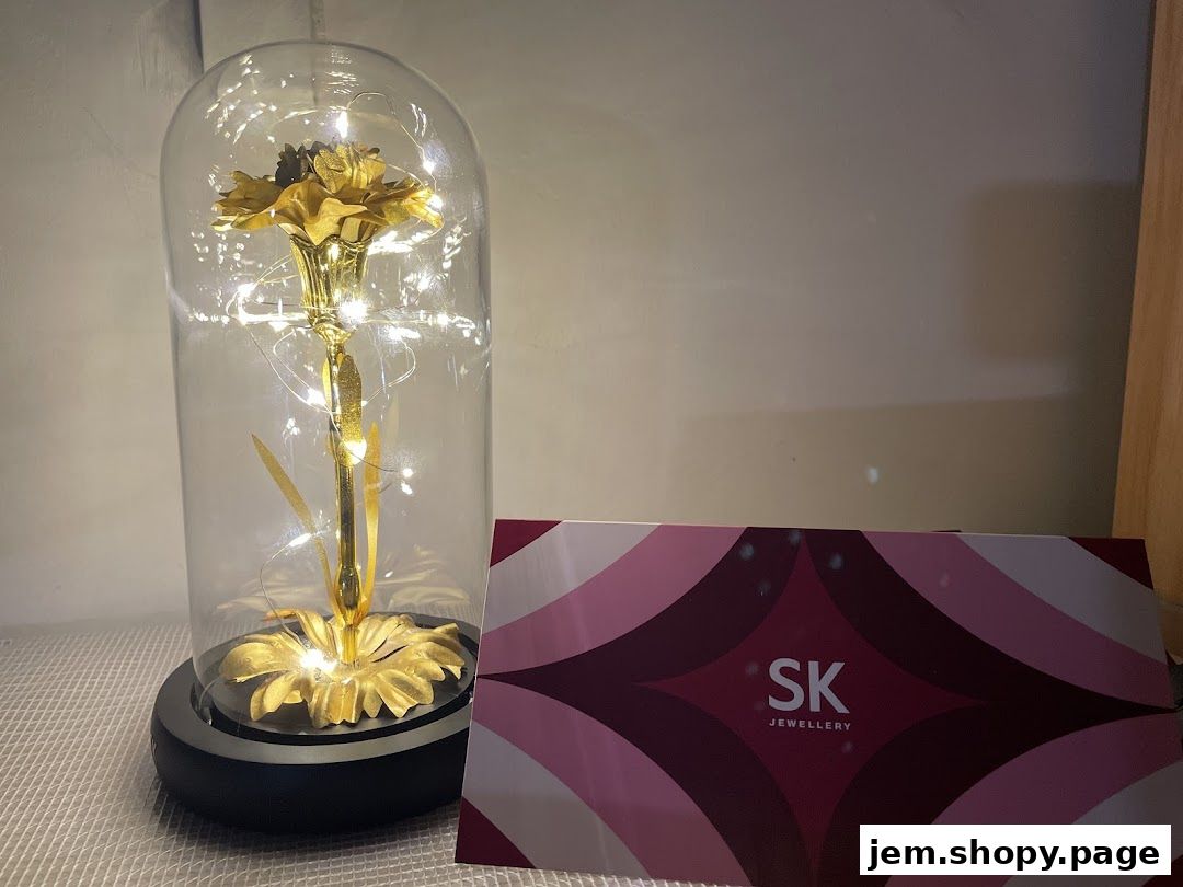 A golden rose under a glass dome with fairy lights next to SK Jewellery branding.