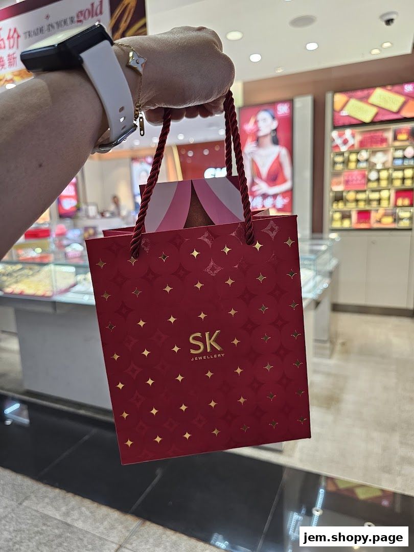 A hand holds a red SK Jewellery shopping bag with gold star patterns.