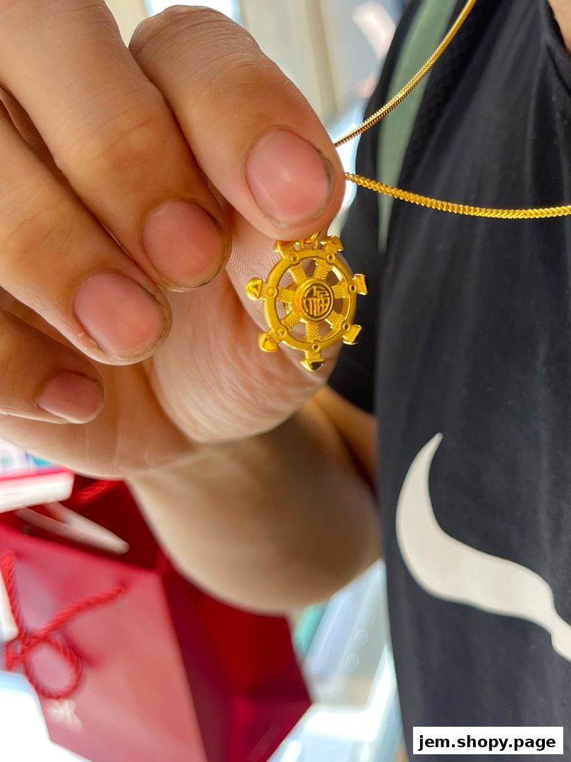 A hand holds a gold pendant with intricate detailing and Chinese characters.