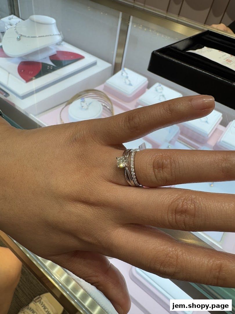 A hand wearing a diamond engagement ring and wedding band in a jewelry store display.