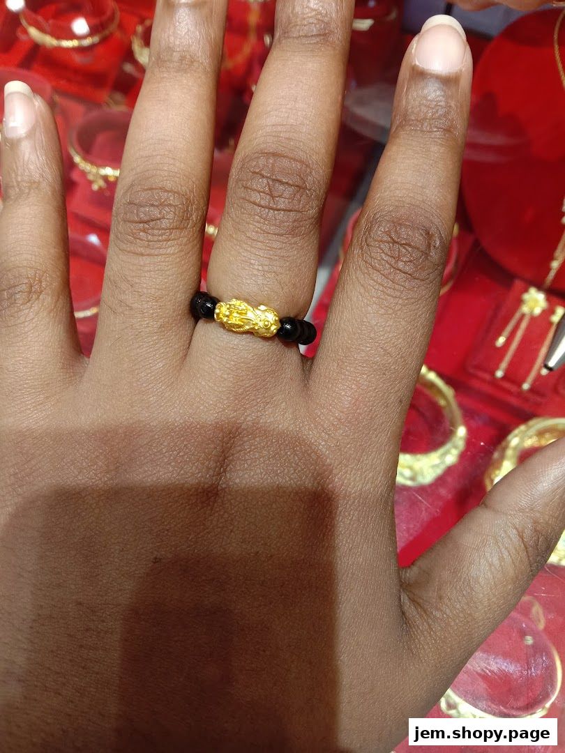 A hand wearing a gold Pixiu charm ring with black beads.