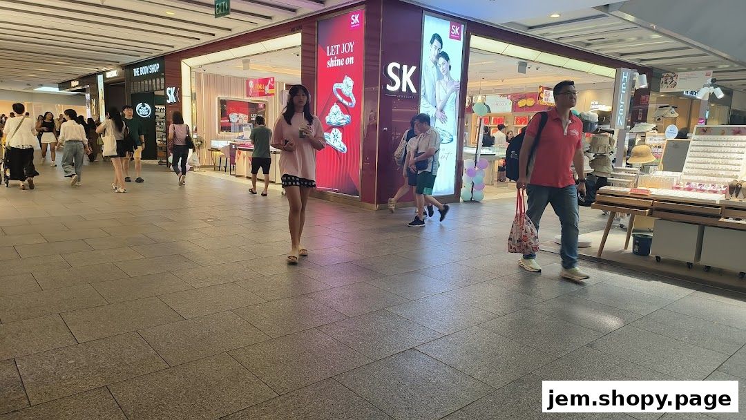 People walking past SK Jewellery Jem store with displays of jewelry and rings.