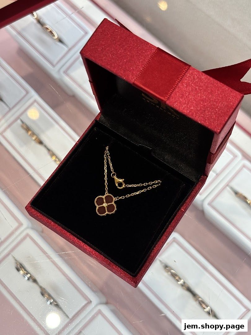A gold necklace with a clover pendant in a red jewelry box.